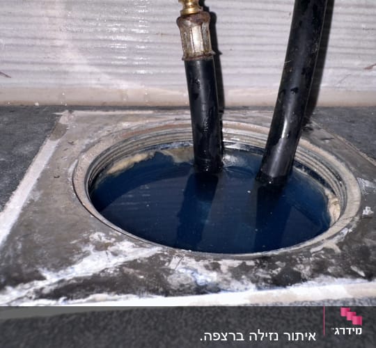 צינורות שחורים בתוך פתח ניקוז עם מים כחולים